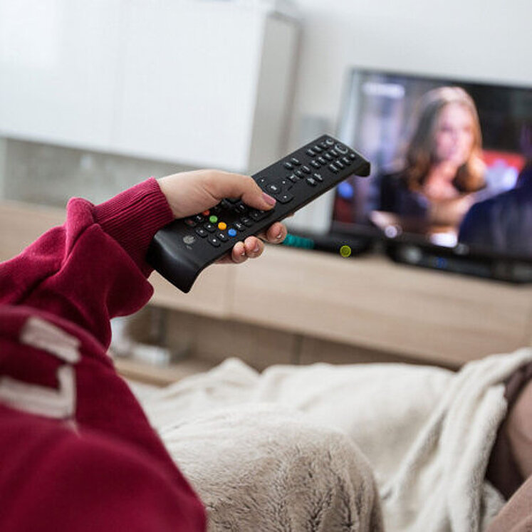 Person mit Fernbedienung vor Fernseher
